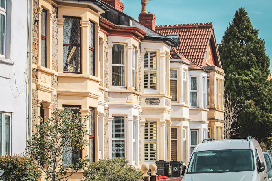 A row of Victorian-style terraced houses with detailed stone and brick facades, bay windows, and pitched red-tile roofs are visible in this exterior shot taken during daytime. The houses feature white