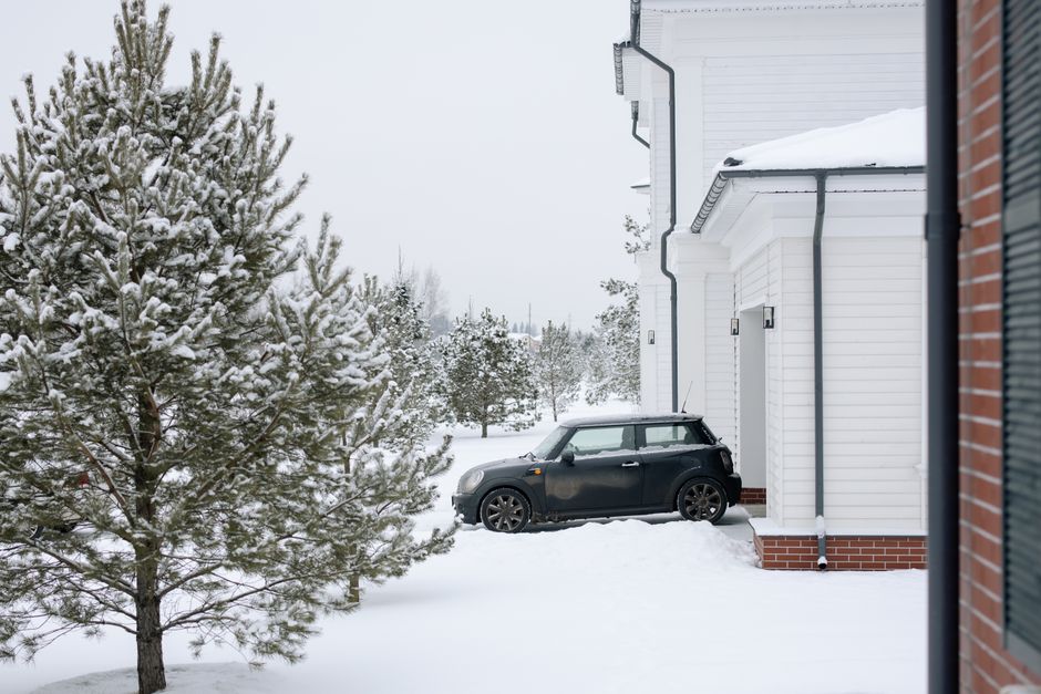 Photograph taken during a home relocation process showing a black Mini Cooper parked on a snow-covered driveway next to a modern white house with brick accents in Mill Hill (NW7). The vehicle is posit