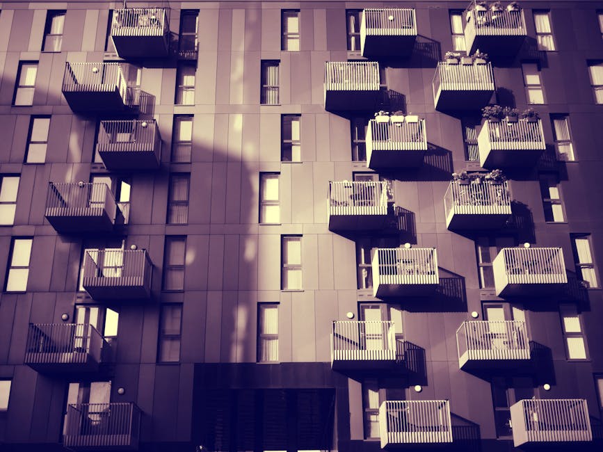 Close-up view of a modern residential building facade with three small rounded balconies featuring black metal railings and coral-colored undersides. The building has large glass doors and windows fra
